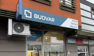 Szyld salonu okien i drzwi "BUDVAR" z logo, klimatyzatorem i napisem "OKNA DRZWI ROLETY".