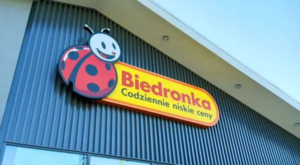 Logo Biedronki z charakterystyczną biedronką na tle nowoczesnej fasady sklepu.