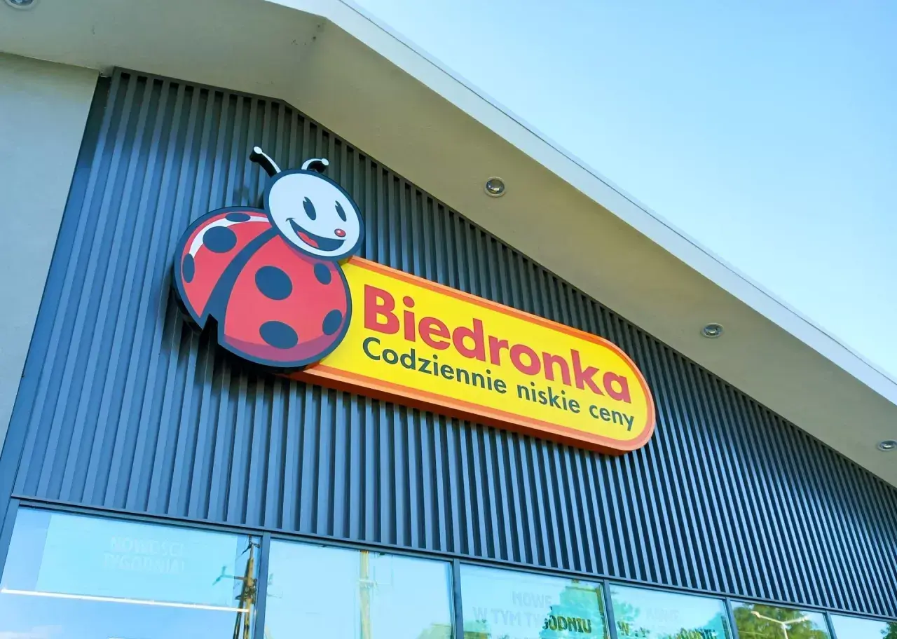 Logo Biedronki z charakterystyczną biedronką na tle nowoczesnej fasady sklepu.