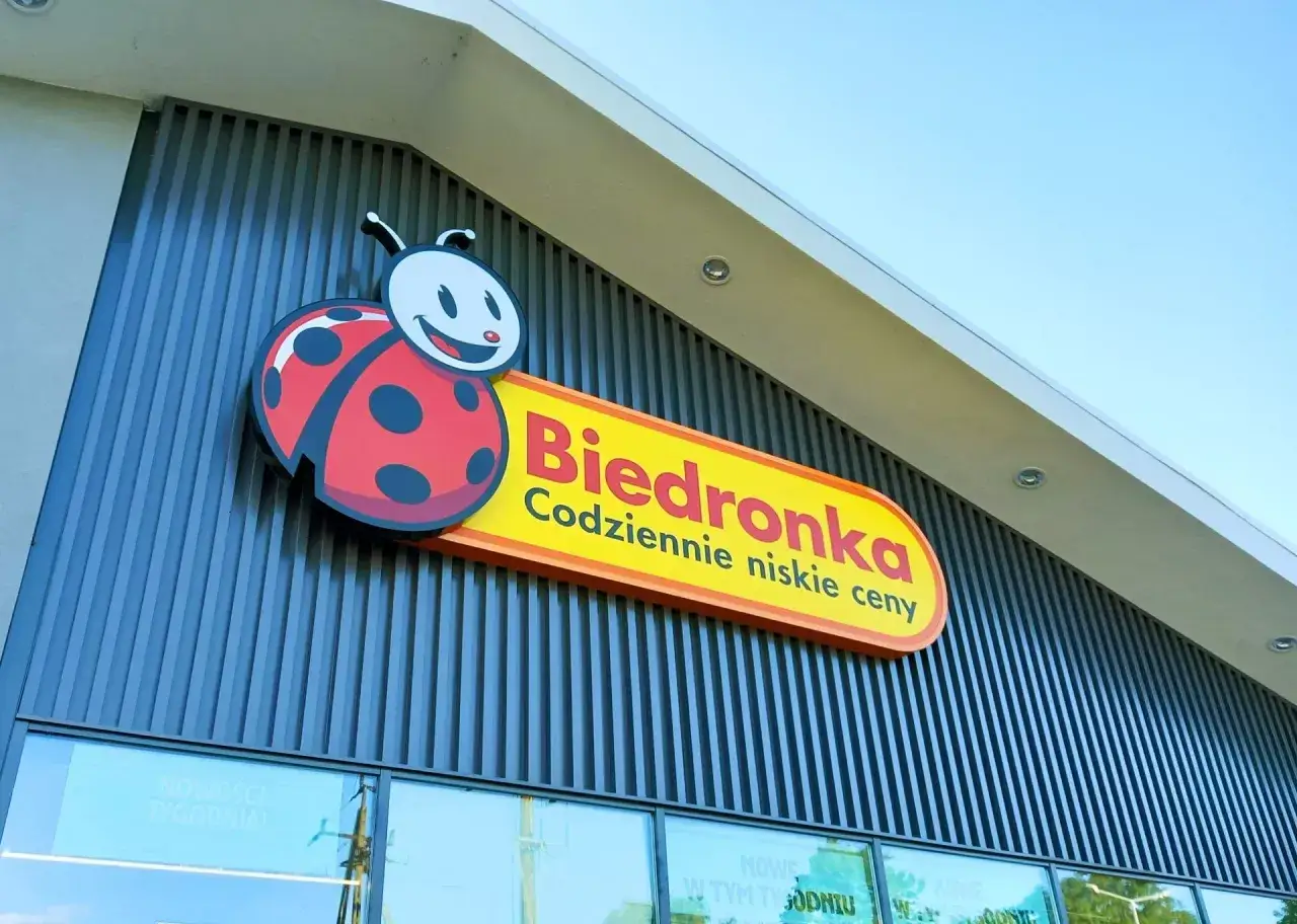 Logo Biedronki z charakterystyczną biedronką na tle nowoczesnej fasady sklepu.